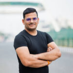 Outdoor portrait image  of a young man of Indian origin with folded hands wearing black T-Shirt and eyeglasses.